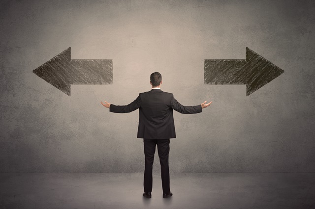 Business man taking a decision while standing in front of two grungy arrows on wall concept